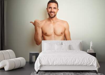 Young handsome shirtless man over isolated background smiling with happy face looking and pointing to the side with thumb up. Wall mural