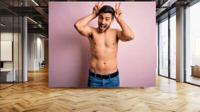 Young handsome strong man with beard shirtless standing over isolated pink background Posing funny and crazy with fingers on head as bunny ears, smiling cheerful Wall mural