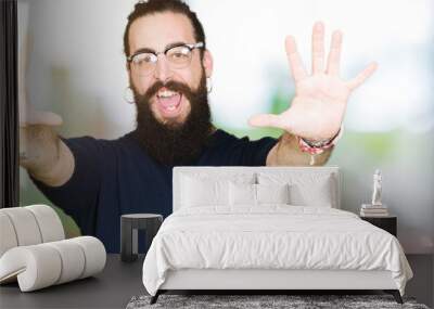 Young hipster man with long hair and beard wearing glasses showing and pointing up with fingers number ten while smiling confident and happy. Wall mural