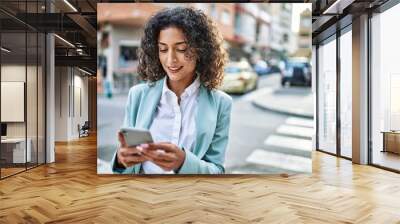 Young hispanic business woman wearing professional look smiling confident at the city using smartphone Wall mural