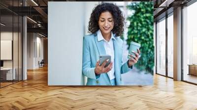 Young hispanic business woman wearing professional look smiling confident at the city using smartphone Wall mural