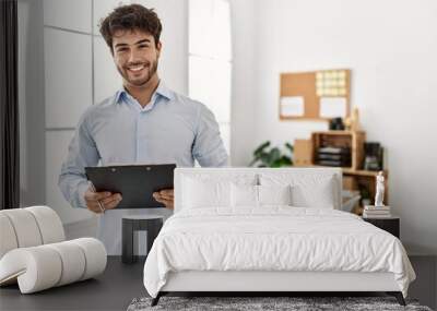 Young hispanic businessman smiling happy holding clipboard at the office. Wall mural