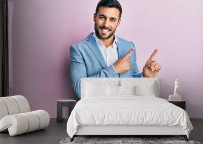 Young hispanic businessman wearing business jacket smiling and looking at the camera pointing with two hands and fingers to the side. Wall mural