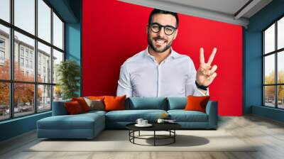 Young hispanic businessman wearing shirt and glasses showing and pointing up with fingers number two while smiling confident and happy. Wall mural