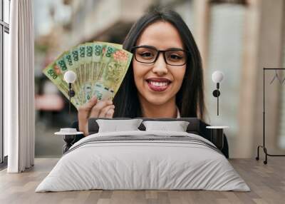 Young hispanic businesswoman holding argentina pesos banknotes at the city. Wall mural