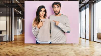 Young hispanic couple wearing casual clothes surprised pointing with finger to the side, open mouth amazed expression. Wall mural