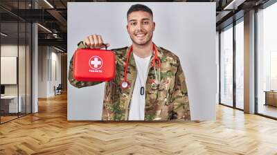 Young hispanic doctor wearing camouflage army uniform holding first aid kit looking positive and happy standing and smiling with a confident smile showing teeth Wall mural