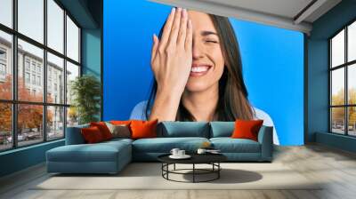 Young hispanic girl covering half face with hand winking looking at the camera with sexy expression, cheerful and happy face. Wall mural