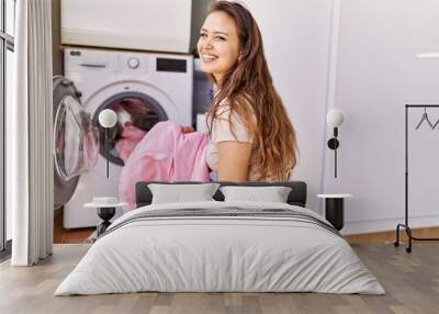 Young hispanic girl doing laundry putting clothes in washing machine at home Wall mural