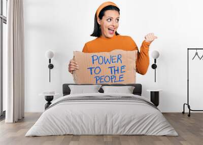 Young hispanic girl holding power to the people banner pointing thumb up to the side smiling happy with open mouth Wall mural