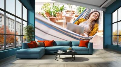 Young hispanic girl using laptop lying on hammock at the terrace. Wall mural