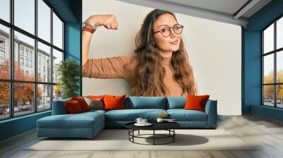 Young hispanic girl wearing casual clothes and glasses strong person showing arm muscle, confident and proud of power Wall mural