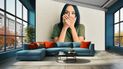 Young hispanic girl wearing casual t shirt shocked covering mouth with hands for mistake. secret concept. Wall mural