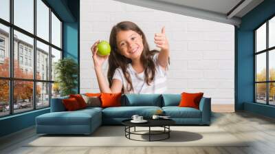 Young hispanic kid sitting on the table eating fresh green apple happy with big smile doing ok sign, thumb up with fingers, excellent sign Wall mural