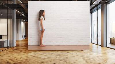 Young hispanic kid stading over white brick wall looking to side, relax profile pose with natural face with confident smile. Wall mural