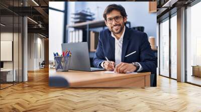 Young hispanic man business worker using laptop write on document at office Wall mural