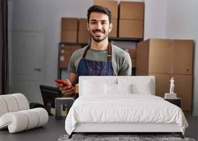 Young hispanic man business worker using smartphone holding packages at storehouse Wall mural