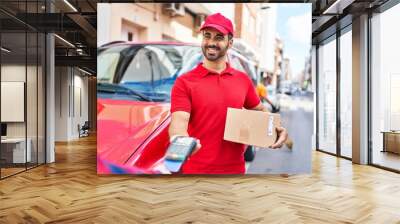 Young hispanic man courier charging with dataphone and credit card at street Wall mural