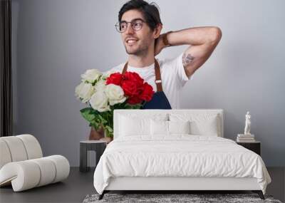 Young hispanic man holding bouquet of white and red roses smiling confident touching hair with hand up gesture, posing attractive and fashionable Wall mural