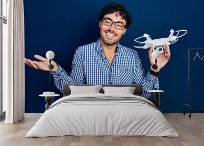 Young hispanic man holding drone celebrating achievement with happy smile and winner expression with raised hand Wall mural