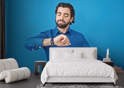 Young hispanic man looking watch over isolated blue background Wall mural