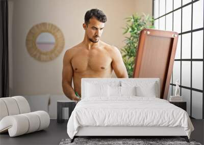 Young hispanic man measuring waist looking on mirror at bedroom Wall mural