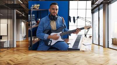 Young hispanic man musician smiling confident playing electrical guitar at music studio Wall mural