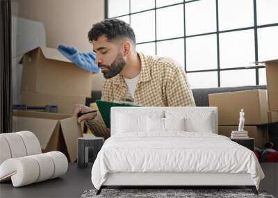 Young hispanic man sitting on sofa checking packages at new home Wall mural