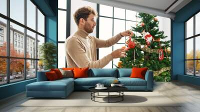 Young hispanic man smiling confident decorating christmas tree at home Wall mural