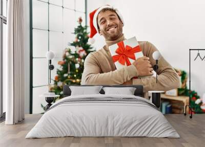 Young hispanic man smiling confident holding christmas gift at home Wall mural