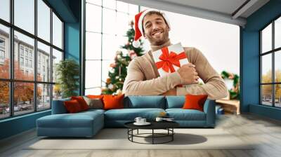 Young hispanic man smiling confident holding christmas gift at home Wall mural