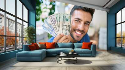 Young hispanic man smiling happy holding american dollars at the terrace. Wall mural