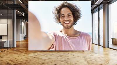 Young hispanic man smiling happy make selfie by the camera standing at the beach. Wall mural