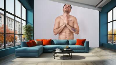 Young hispanic man standing shirtless wearing underware begging and praying with hands together with hope expression on face very emotional and worried. begging. Wall mural