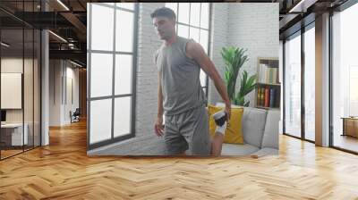 Young hispanic man stretching in a modern living room, dressed in casual athleisure wear Wall mural