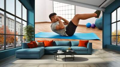 Young hispanic man training abs exercise at sport center Wall mural