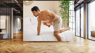 Young hispanic man training arm with dumbbell at bedroom Wall mural