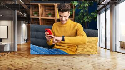 Young hispanic man using smartphone and looking watch at home Wall mural