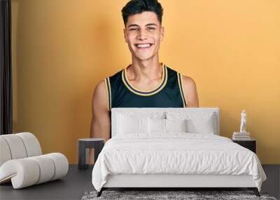 Young hispanic man wearing basketball uniform with a happy and cool smile on face. lucky person. Wall mural