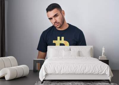 Young hispanic man wearing bitcoin t shirt looking sleepy and tired, exhausted for fatigue and hangover, lazy eyes in the morning. Wall mural