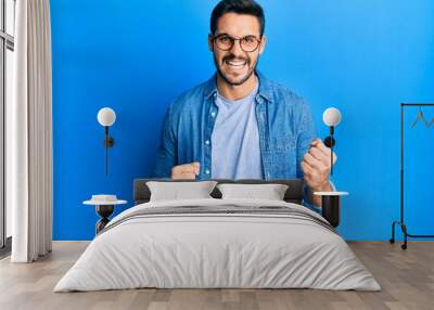 Young hispanic man wearing casual clothes and glasses celebrating surprised and amazed for success with arms raised and eyes closed Wall mural