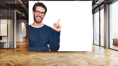 Young hispanic man wearing casual clothes and glasses with a big smile on face, pointing with hand and finger to the side looking at the camera. Wall mural