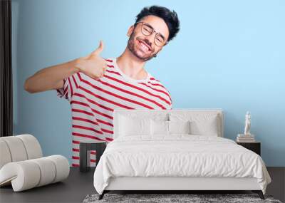 Young hispanic man wearing casual clothes doing happy thumbs up gesture with hand. approving expression looking at the camera showing success. Wall mural