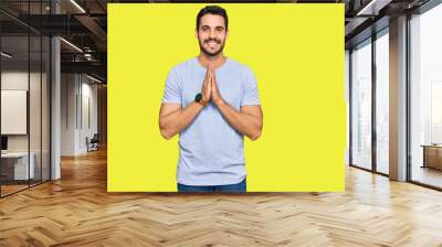 Young hispanic man wearing casual clothes praying with hands together asking for forgiveness smiling confident. Wall mural