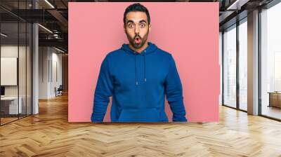 Young hispanic man wearing casual clothes scared and amazed with open mouth for surprise, disbelief face Wall mural