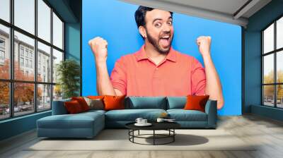 Young hispanic man wearing casual clothes screaming proud, celebrating victory and success very excited with raised arms Wall mural