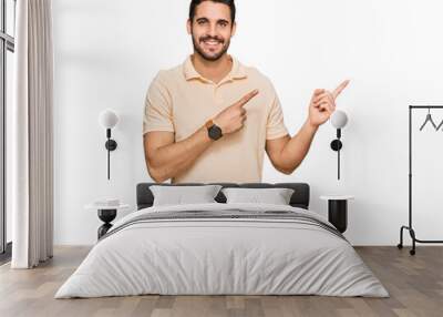 Young hispanic man wearing casual clothes smiling and looking at the camera pointing with two hands and fingers to the side. Wall mural