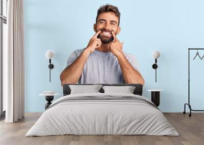 Young hispanic man wearing casual clothes smiling with open mouth, fingers pointing and forcing cheerful smile Wall mural