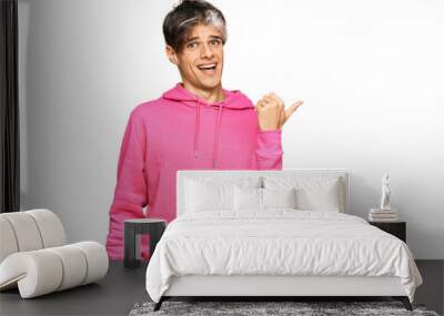 Young hispanic man wearing casual pink sweatshirt smiling with happy face looking and pointing to the side with thumb up. Wall mural