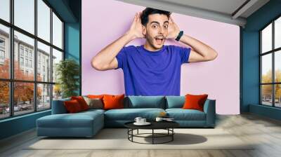 Young hispanic man wearing casual t shirt smiling cheerful playing peek a boo with hands showing face. surprised and exited Wall mural